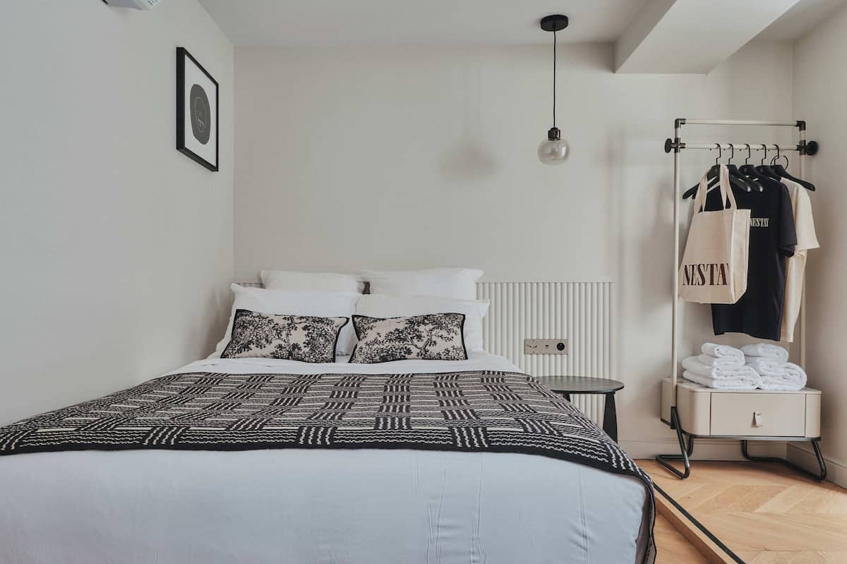 A minimalist bedroom with a bed, a hanging light, a radiator, and a clothing rack with towels.