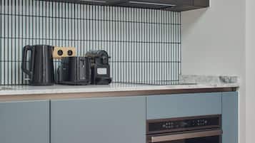 Ett modernt kök med gråa skåp, en inbyggd ugn och en kaffebryggare på bänkskivan.