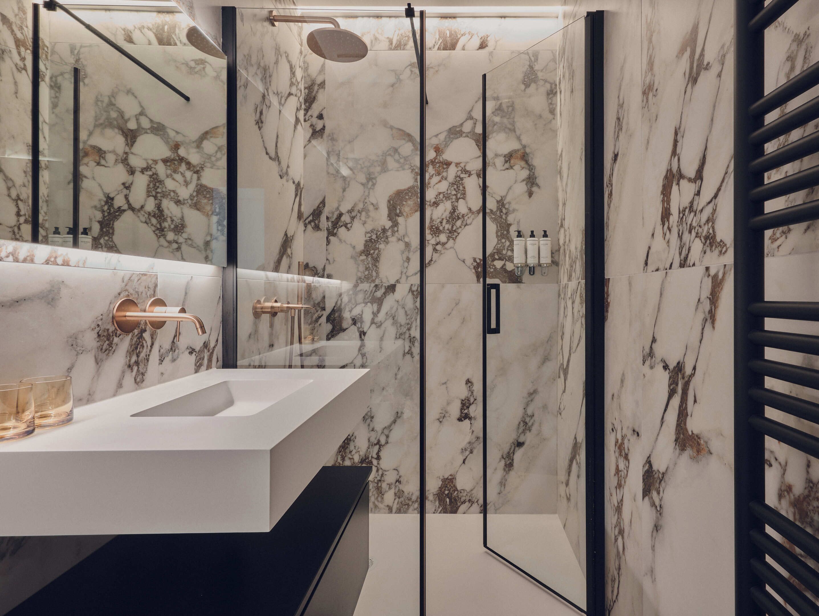 A modern bathroom with a marble vanity, a glass shower enclosure, and a black towel rack.