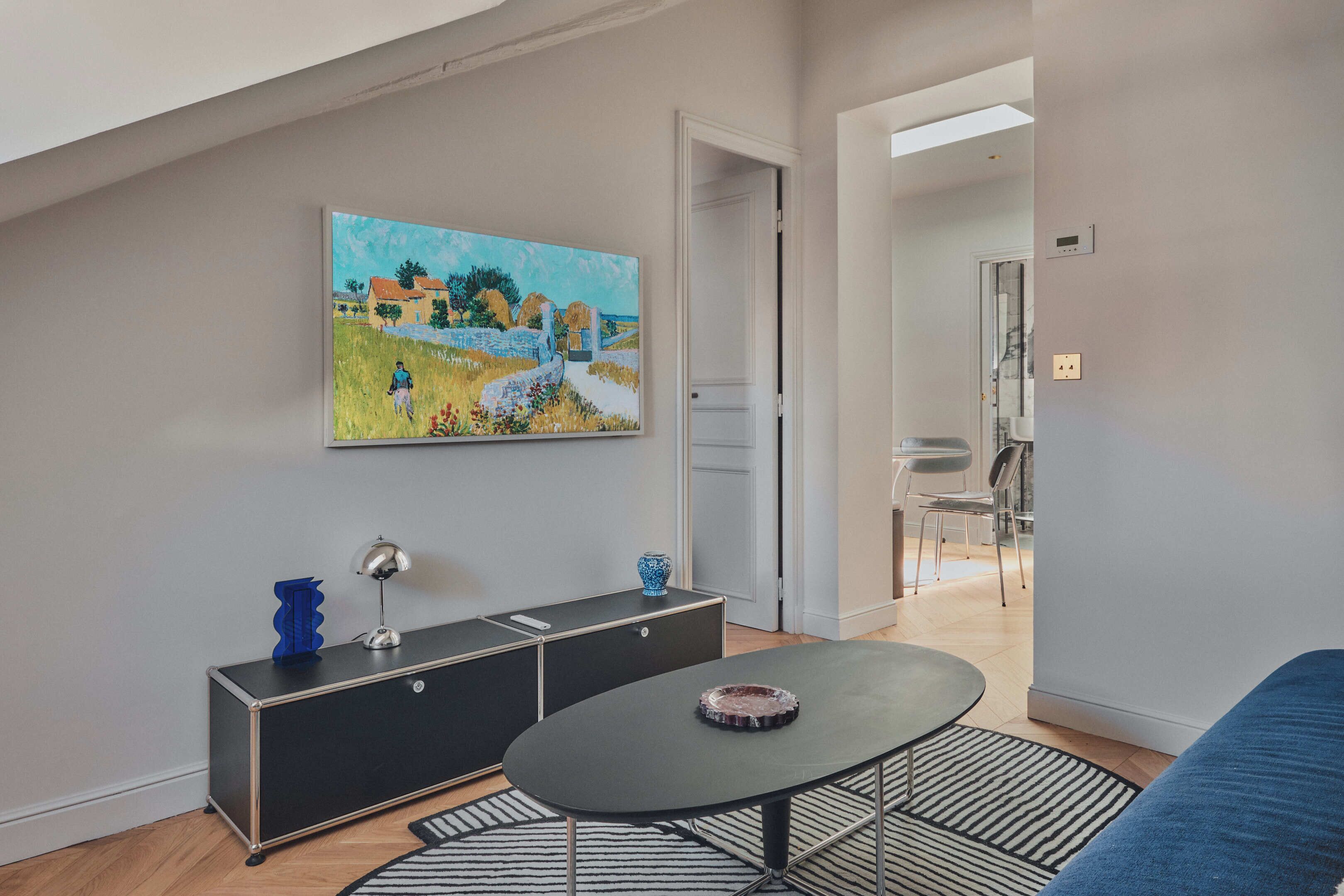 Ein modernes Wohnzimmer mit einer schwarzen Couch, einem runden Couchtisch, einem Gemälde an der Wand und einer schwarzen Konsole mit Dekorationselementen.