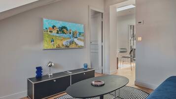 Ein modernes Wohnzimmer mit einer schwarzen Couch, einem runden Couchtisch, einem Gemälde an der Wand und einer schwarzen Konsole mit Dekorationselementen.