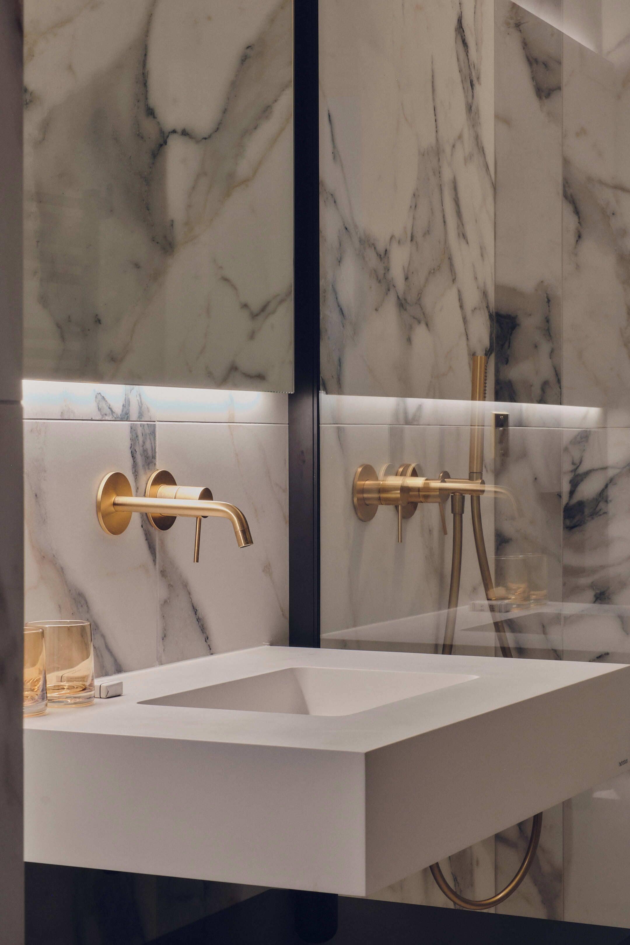 A modern bathroom with a marble wall, a white sink, and gold fixtures.