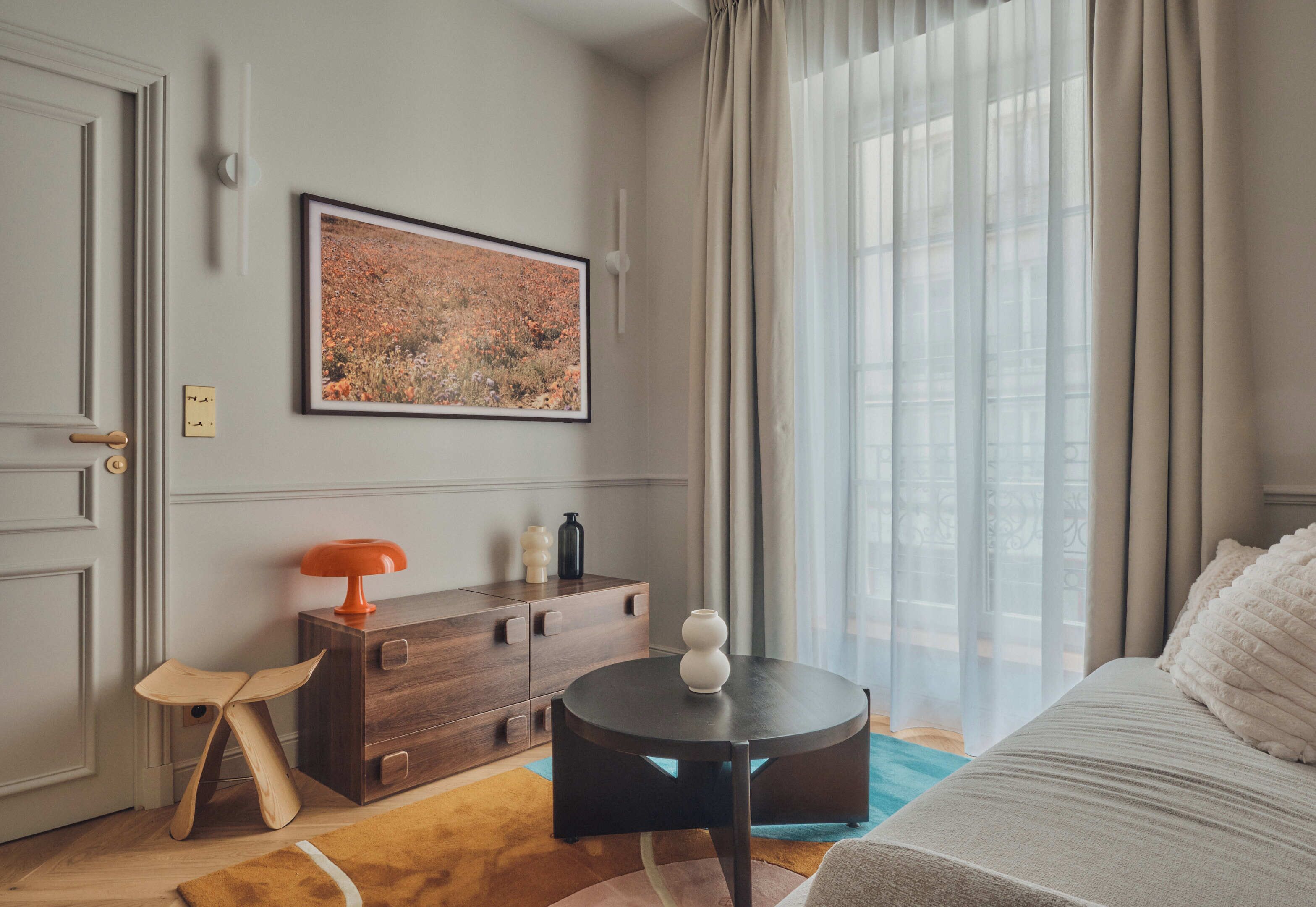 A modern room with a bed, a small round table with a vase, a wooden chair, a dresser, and a framed picture on the wall.