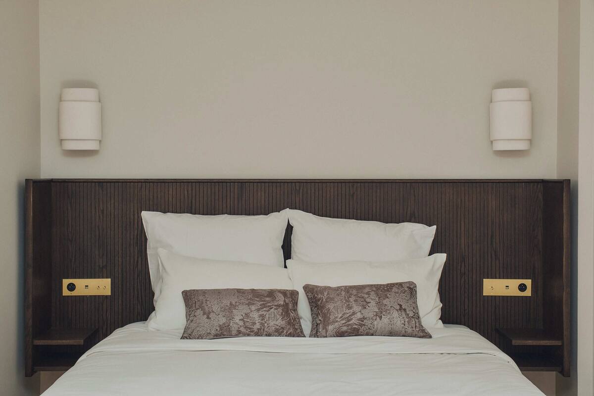 A neatly made bed with white and patterned pillows, a dark wood headboard, and two bedside tables with wall-mounted lamps.