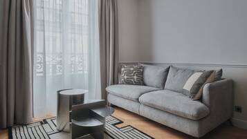 Ein modernes Wohnzimmer mit einem grauen Sofa, gemusterten Kissen, einem kleinen Beistelltisch und einem geometrischen Teppich.