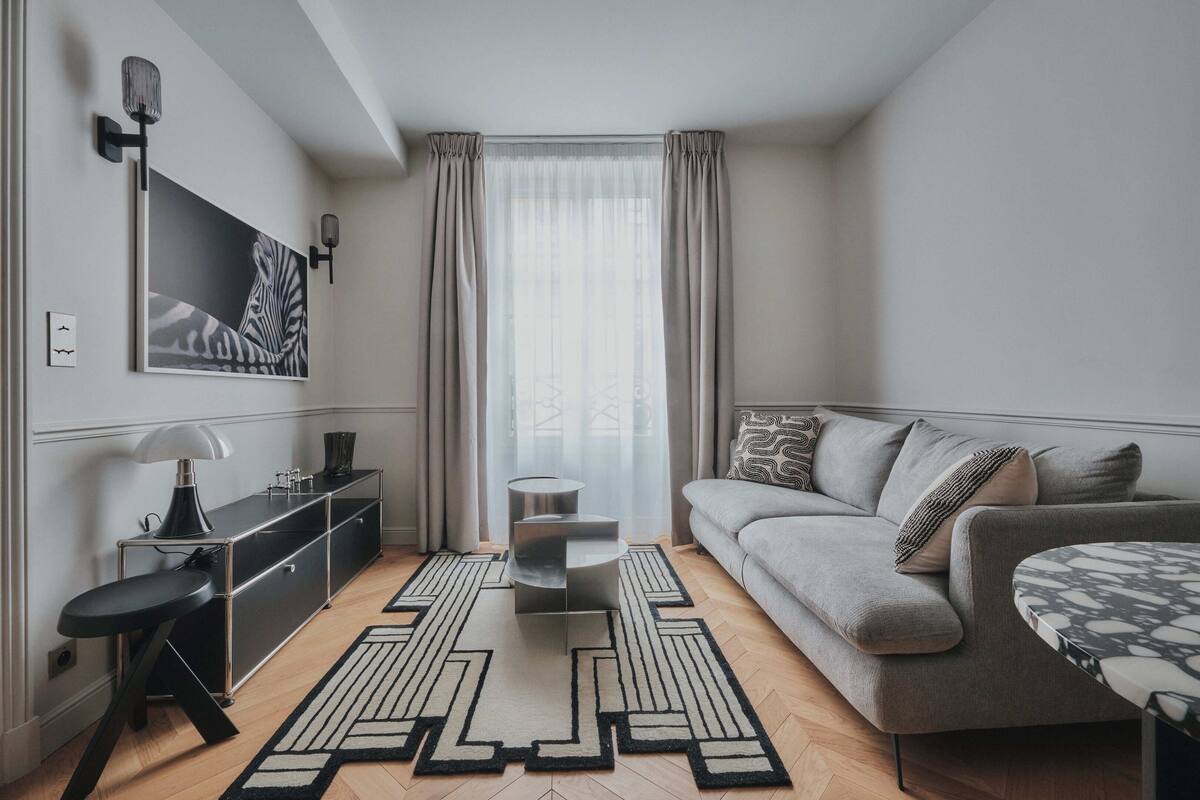 A modern living room with a grey sofa, a black and white patterned coffee table, a black floor lamp, and a black and white rug.