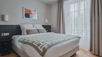 A modern bedroom with a large bed, a headboard, a wall-mounted light, and a window with curtains.
