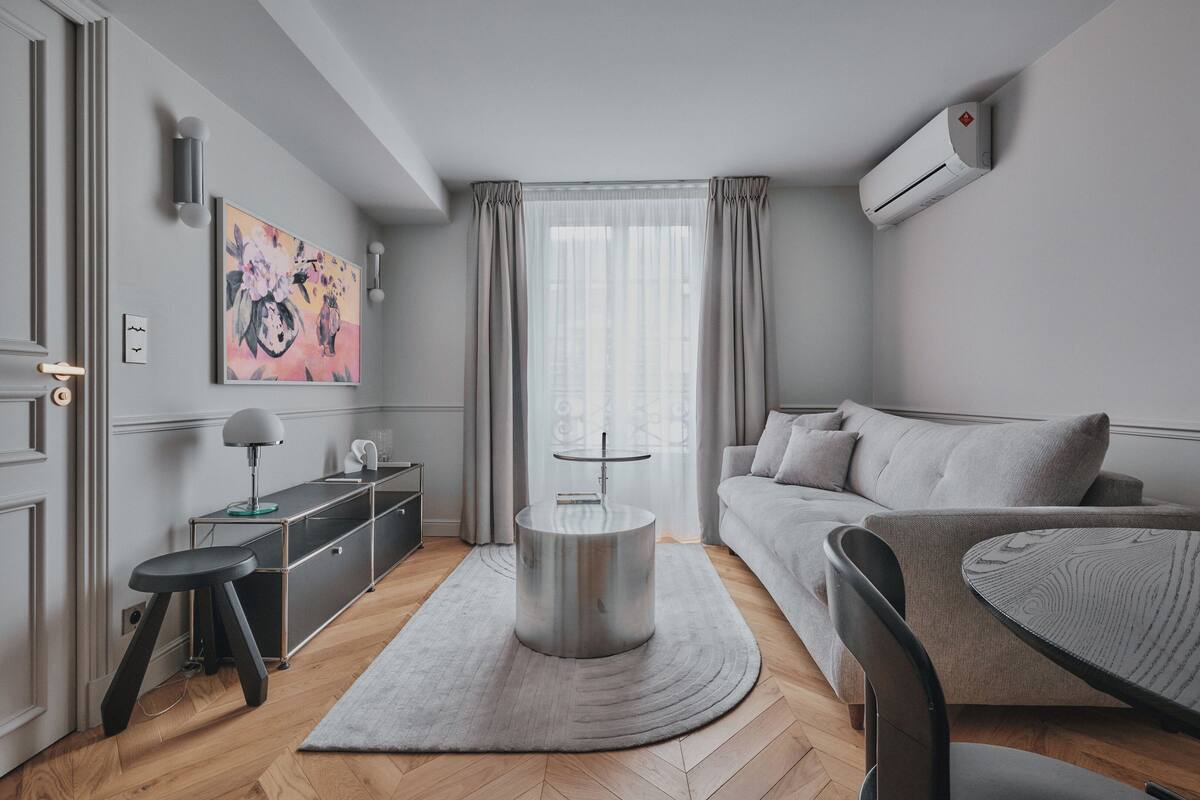 A modern living room with a grey sofa, a round coffee table, a grey rug, a side table, a lamp, and a painting on the wall.