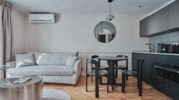 A modern living room with a sofa, dining table, chairs, and a kitchen area with a stove and cabinets.