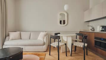 Una sala moderna con un sofá, una mesa redonda y dos sillas. Se observa un área de cocina con estufa y lavaplatos.