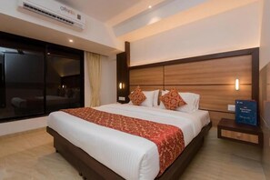A hotel room with a large bed, a nightstand, a wall-mounted air conditioner, and a window with curtains. - Hotel Mourya Residency (Navi Mumbai)