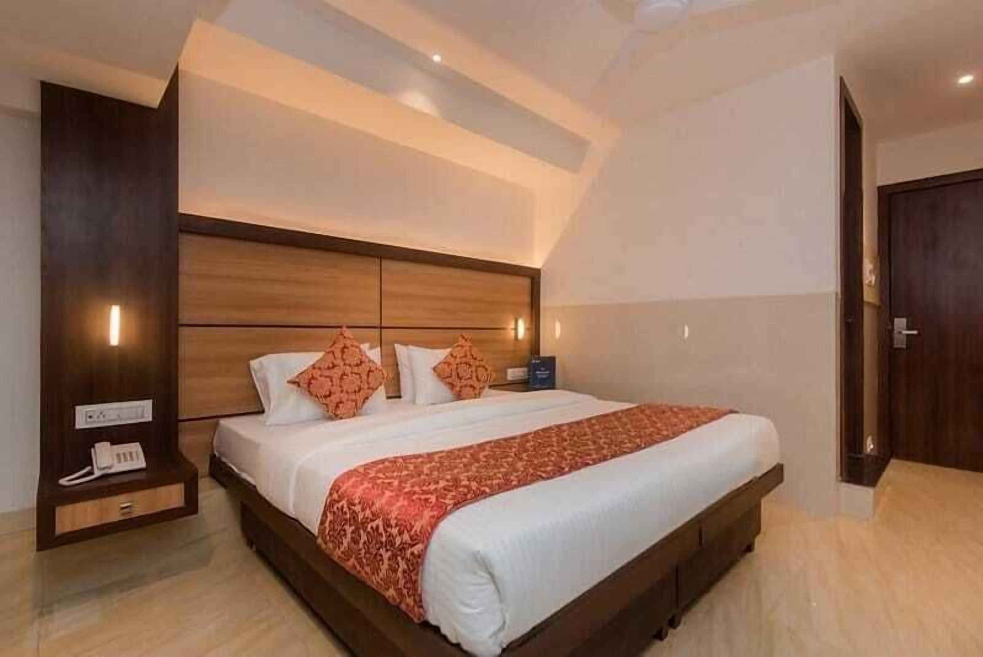 A hotel room with a large bed, wooden headboard, bedside table with a phone, and a door to the right.