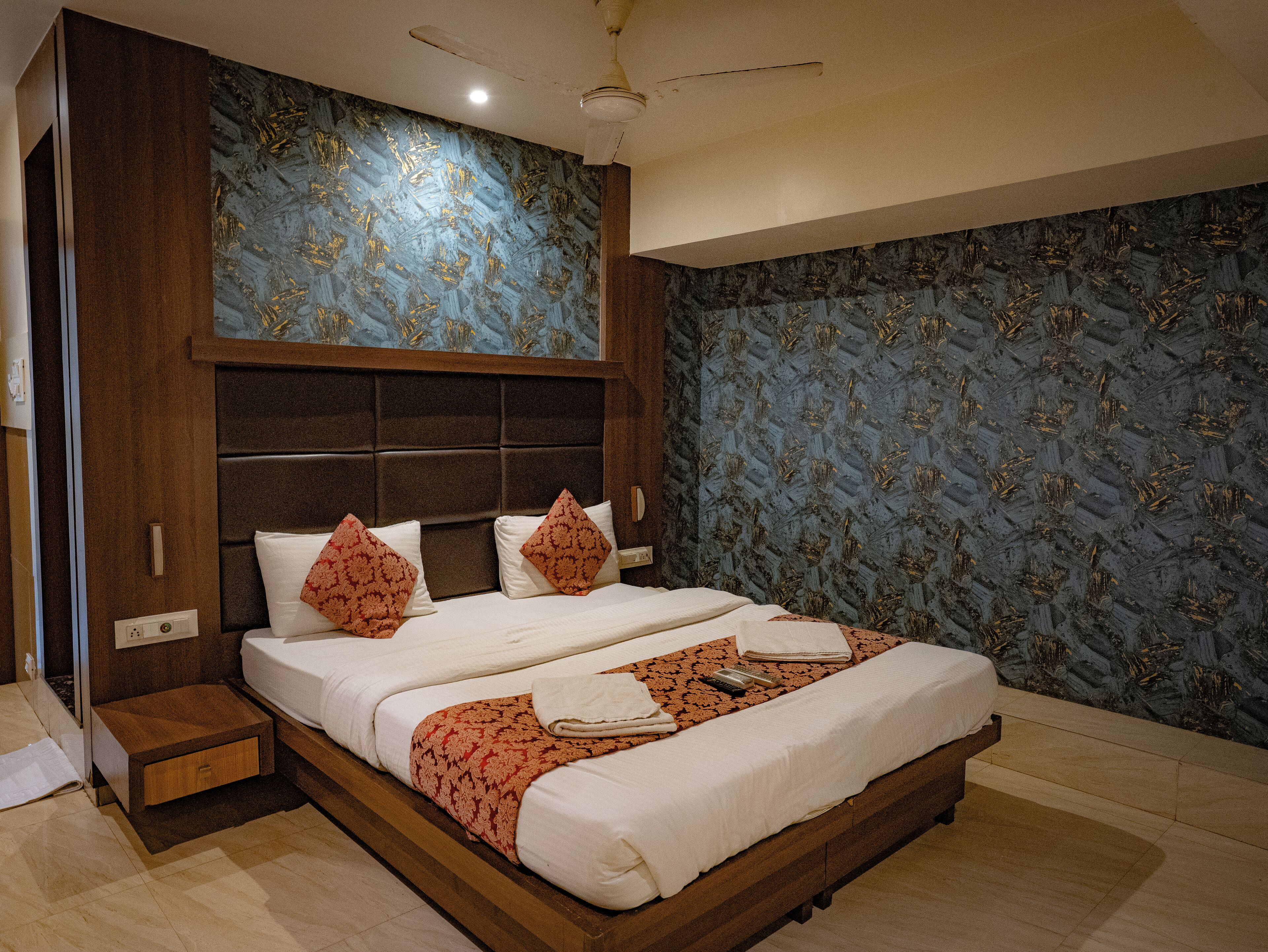 A hotel room with a large bed, wooden headboard, and patterned wallpaper.