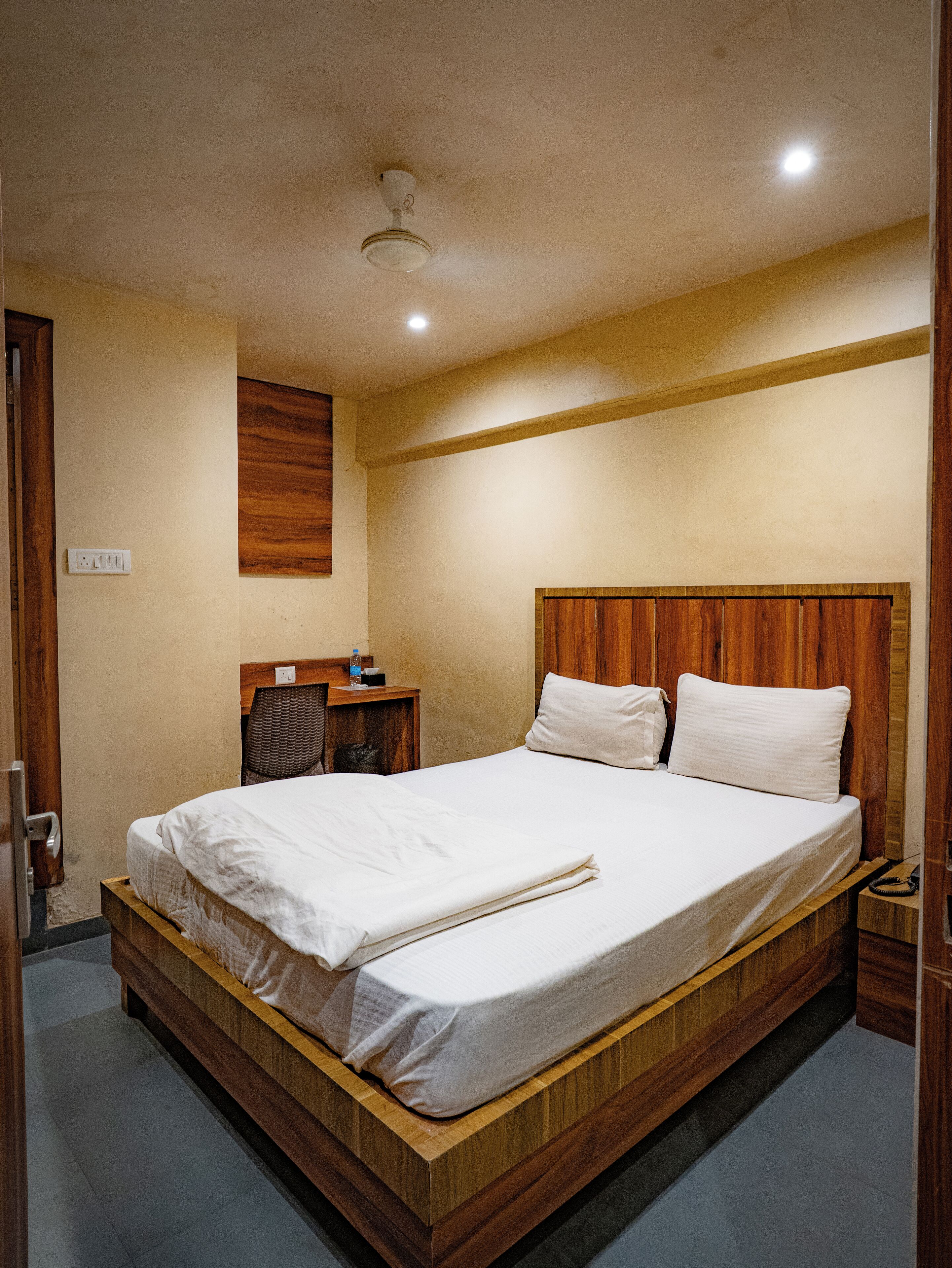 A bedroom with a wooden bed frame, a nightstand, a desk, and a ceiling fan.
