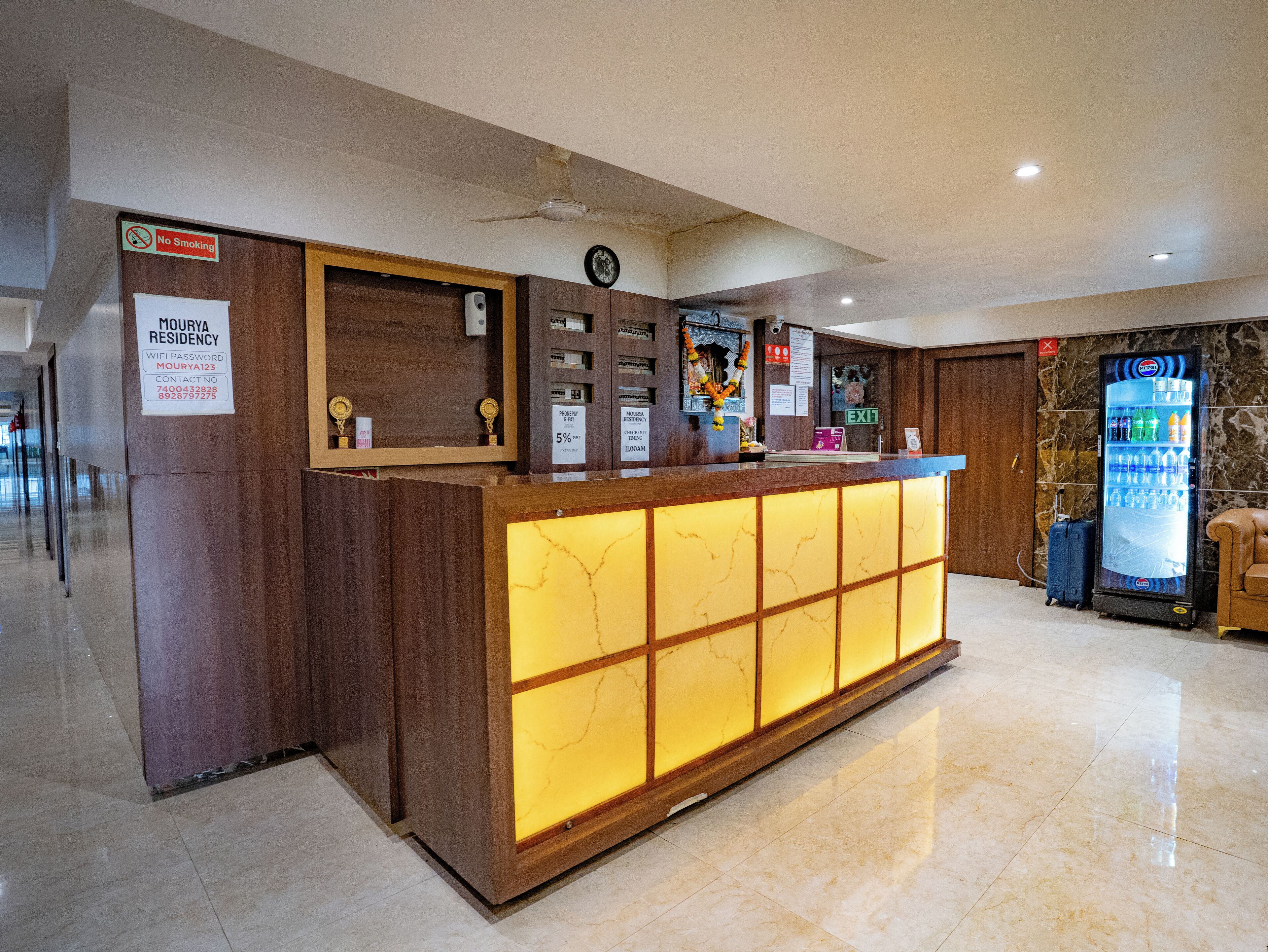A hotel reception desk with a marble floor, a no-smoking sign, a clock, and a vending machine.