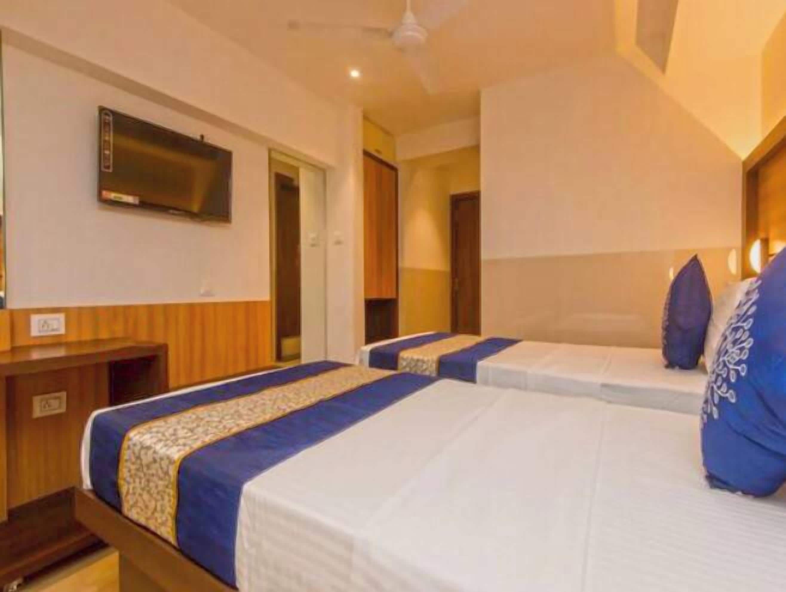 A hotel room with two beds, a TV mounted on the wall, and a wooden desk.