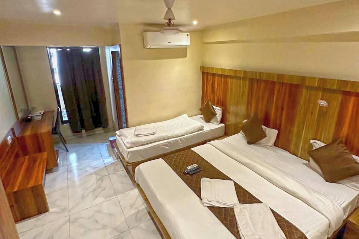 A hotel room with a large bed, a smaller bed, a desk, and an air conditioning unit.