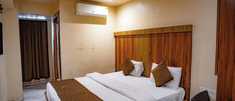 Een hotelkamer met een houten hoofdeinde, een bed met wit en bruin beddengoed, een plafondventilator, een airconditioning en een houten bureau met stoel.