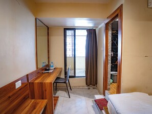 A hotel room with a wooden desk, a chair, a bed, a window with curtains, and a view of the outside. - Hotel Mourya Residency (Navi Mumbai)