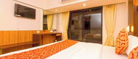 A hotel room with a bed, a desk, a television, and an air conditioning unit.