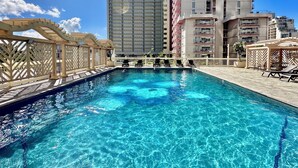 Piscina cristalina con sillas de descanso y una pérgola de madera, rodeada de edificios altos.