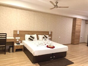 A modern hotel room with a large bed, wooden headboard, bedside tables, and a ceiling fan. - Hotel Silver Oak (Bilaspur)