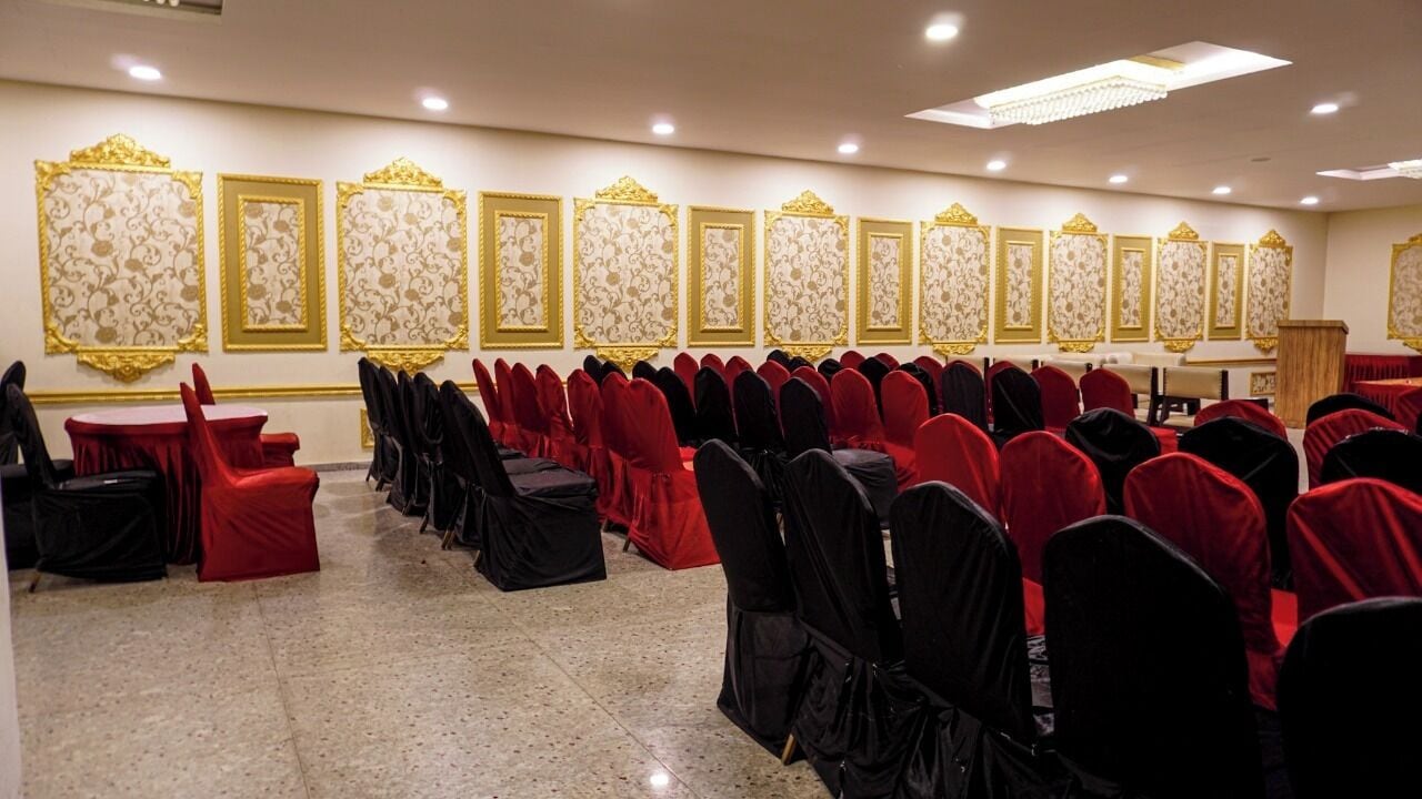 Un salón de banquetes con filas de mesas y sillas, paneles ornamentales en las paredes y un suelo pulido.