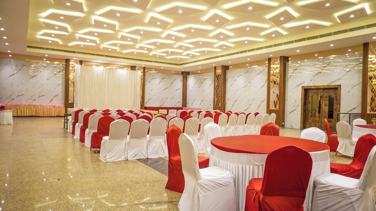 A banquet hall with rows of round tables and chairs, a stage, and a marble wall.