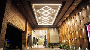 A hallway with wooden paneling, a geometric light fixture on the ceiling, and potted plants along the walls. - Hotel Silver Oak (Bilaspur)