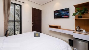 A hotel room with a bed, a TV mounted on the wall, a small shelf with a plant, and a minibar. - Blok M Residence (South Jakarta)