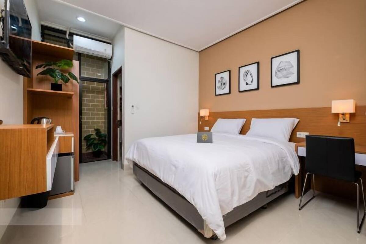 Una habitació d'hotel amb un llit, taules de nit, un escriptori i una cadira. Hi ha llums penjades a la paret i una planta petita sobre l'escriptori.