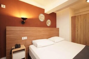 A hotel room with a wooden headboard, a bedside telephone, two wall-mounted lamps, and a wardrobe. - Blok M Residence (South Jakarta)
