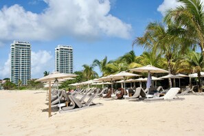 Ein Strand mit Liegestühlen und Sonnenschirmen, Palmen und hohen Gebäuden im Hintergrund.
