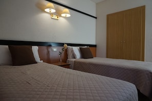 Une chambre d’hôtel avec deux lits, une table de chevet, une lampe et une armoire.