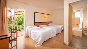 A hotel room with two beds, a wooden desk, a chair, and a balcony with a view of buildings and trees. - Hotel Boutique Can Colom (Lloret de Mar)