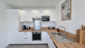 Una cocina moderna con armarios blancos, electrodomésticos de acero inoxidable, una encimera de madera y luces empotradas en el techo.
