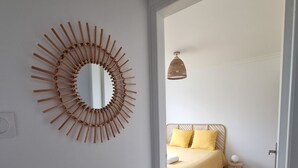 Una habitación con piso de madera, una cama con ropa de cama amarilla, un espejo redondo y una lámpara colgante.