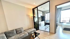Une chambre d’hôtel moderne avec un canapé gris, une petite table basse noire et une grande porte-fenêtre coulissante donnant sur un balcon avec vue sur la ville.