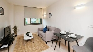 A compact living space with a sofa, a dining table set for two, a TV, and a small side table with a plant.
