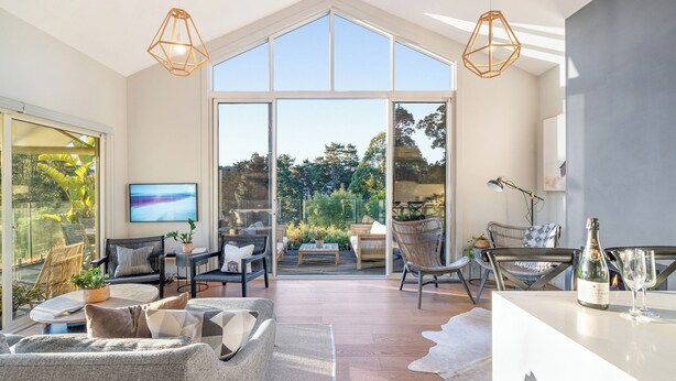 A spacious living area with a large glass door leading to a garden, furnished with sofas, chairs, and a dining table.