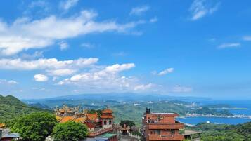 A traditional building with a tiled roof, surrounded by lush greenery and overlooking a coastal area.