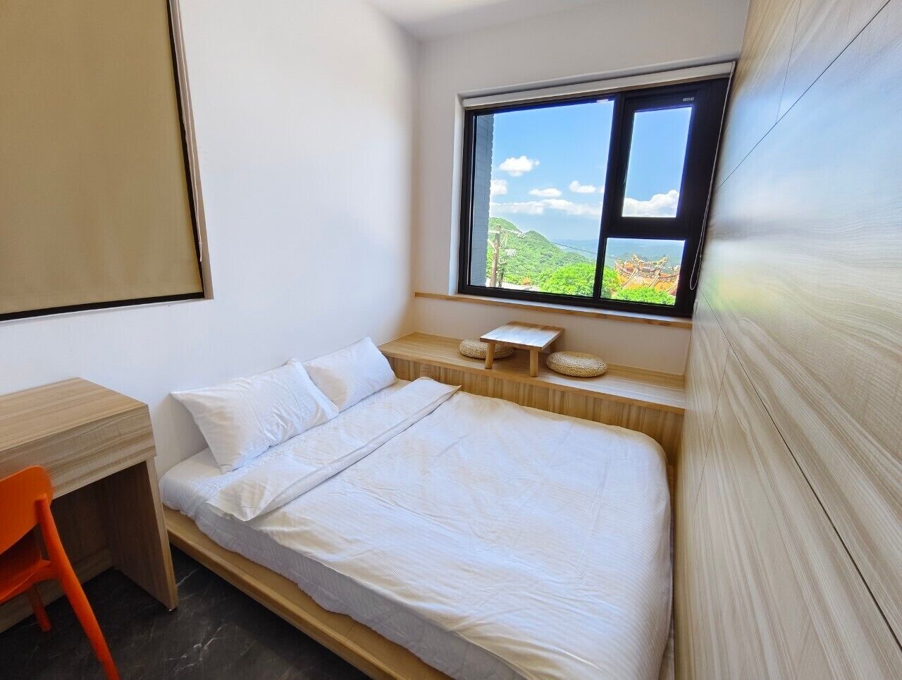 A bedroom with a bed, a desk, and a window with a view of greenery.