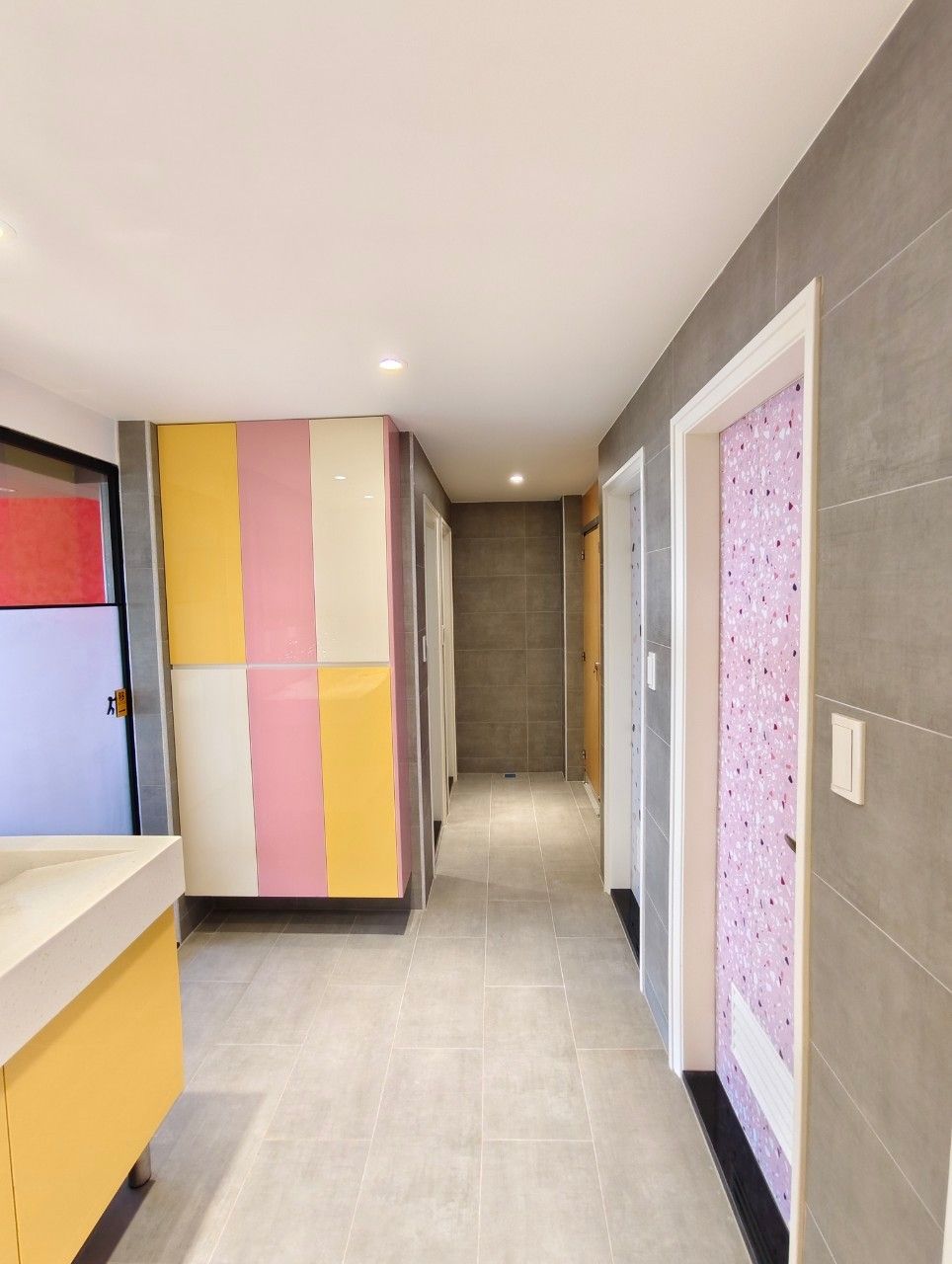 A hallway with a modern design, featuring a combination of neutral and pastel-colored walls, a tiled floor, and a door with a patterned design.