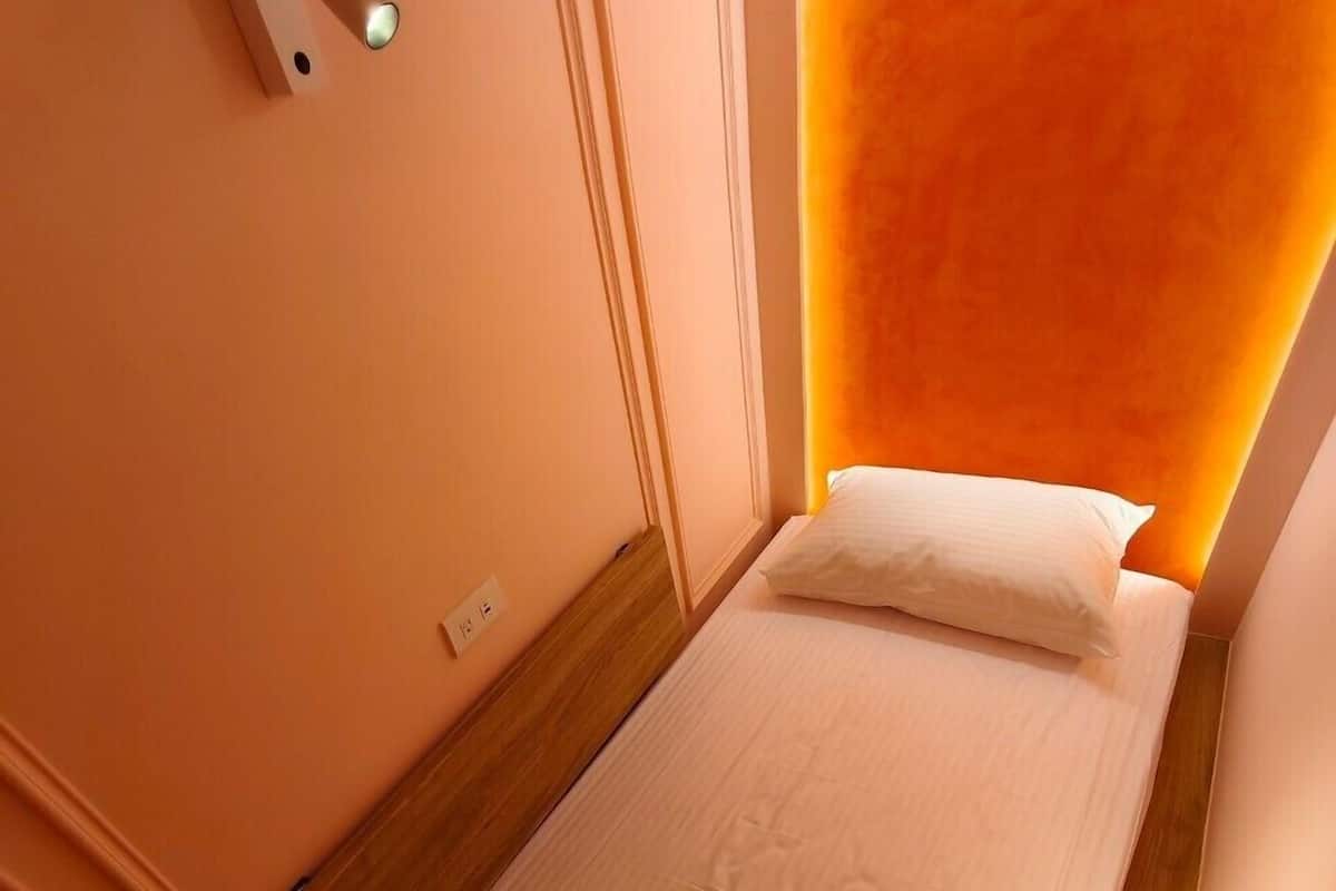 Een eenpersoonsbed met houten hoofdeinde en een wandlamp.