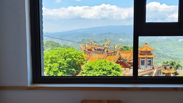 A room with a window overlooking traditional architecture and lush greenery.