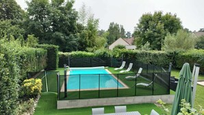 A backyard with a swimming pool, surrounded by a green fence, and a table with chairs. - Magnifique Maison 8/10 Personnes à Rully. Piscine Privée. Terrain de Boule (Rully)