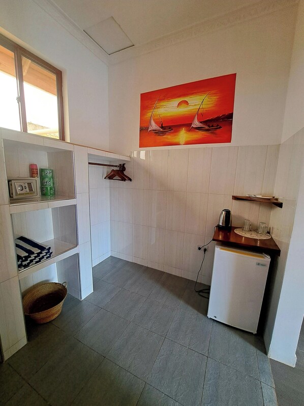 A compact kitchen with white cabinets, a small refrigerator, and a painting of a sunset over the ocean. - Mimi na wewe villa (Nungwi)