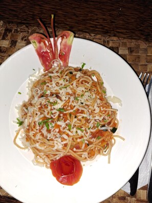 A plate of spaghetti with a garnish of herbs and a decorative tomato slice.
