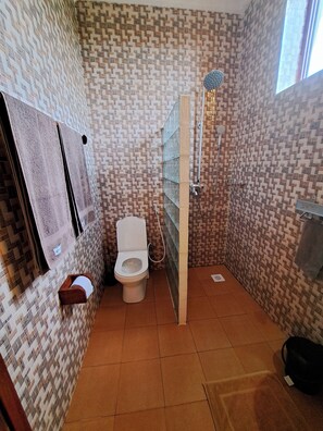 A bathroom with a patterned tile wall, a toilet, a shower, and a towel rack.