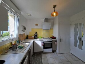Une cuisine compacte équipée d’une cuisinière à gaz, d’une machine à café et d’une fenêtre laissant entrer la lumière naturelle.